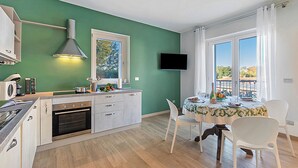 A modern kitchen with a built-in oven, a dining area with a table set for two, and a large window with curtains. - Appartamento Girasole with Terrace, Torino, Italy (Torino)