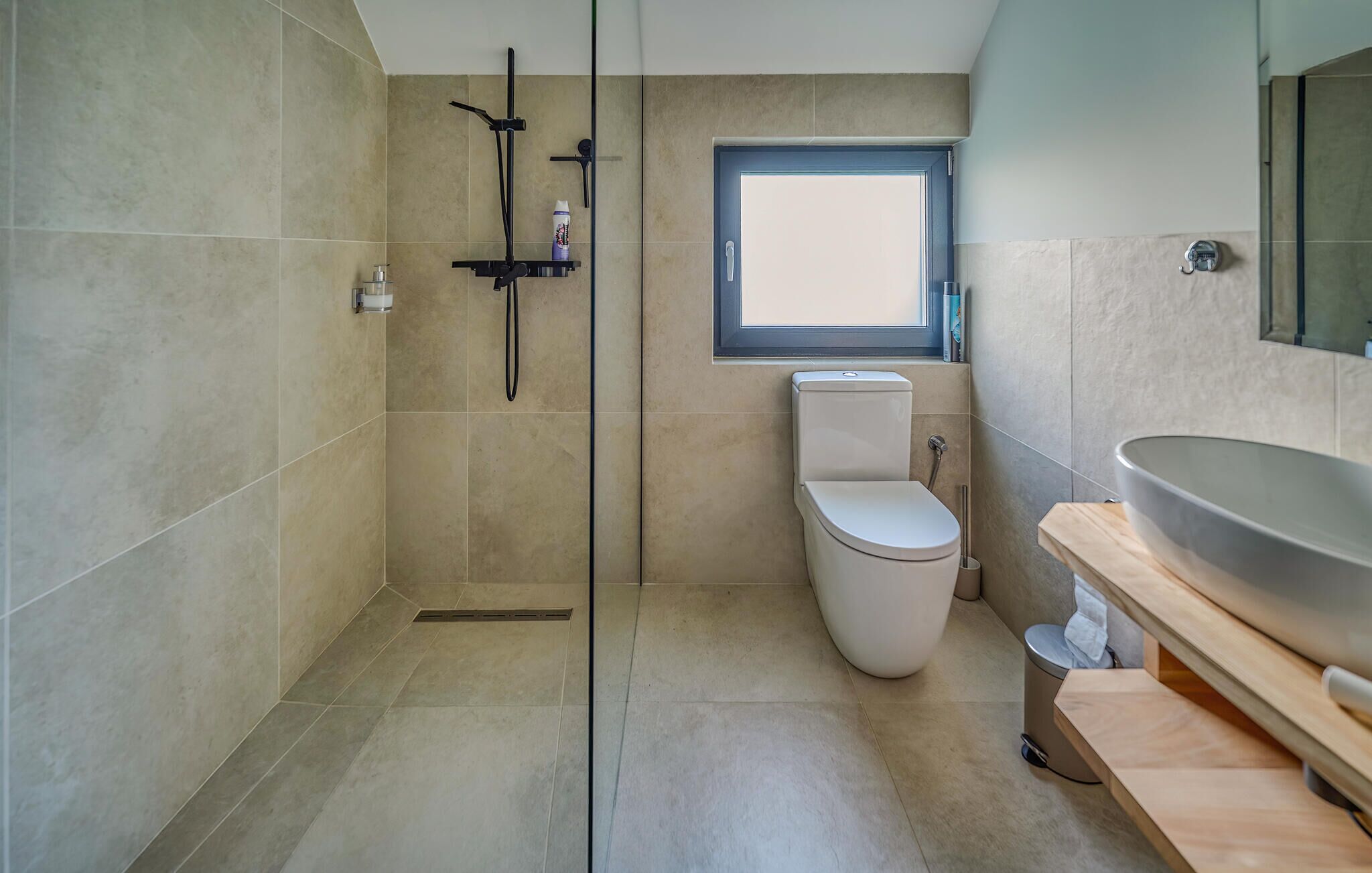 Un baño moderno con cabina de ducha de vidrio, inodoro y un lavamanos grande.