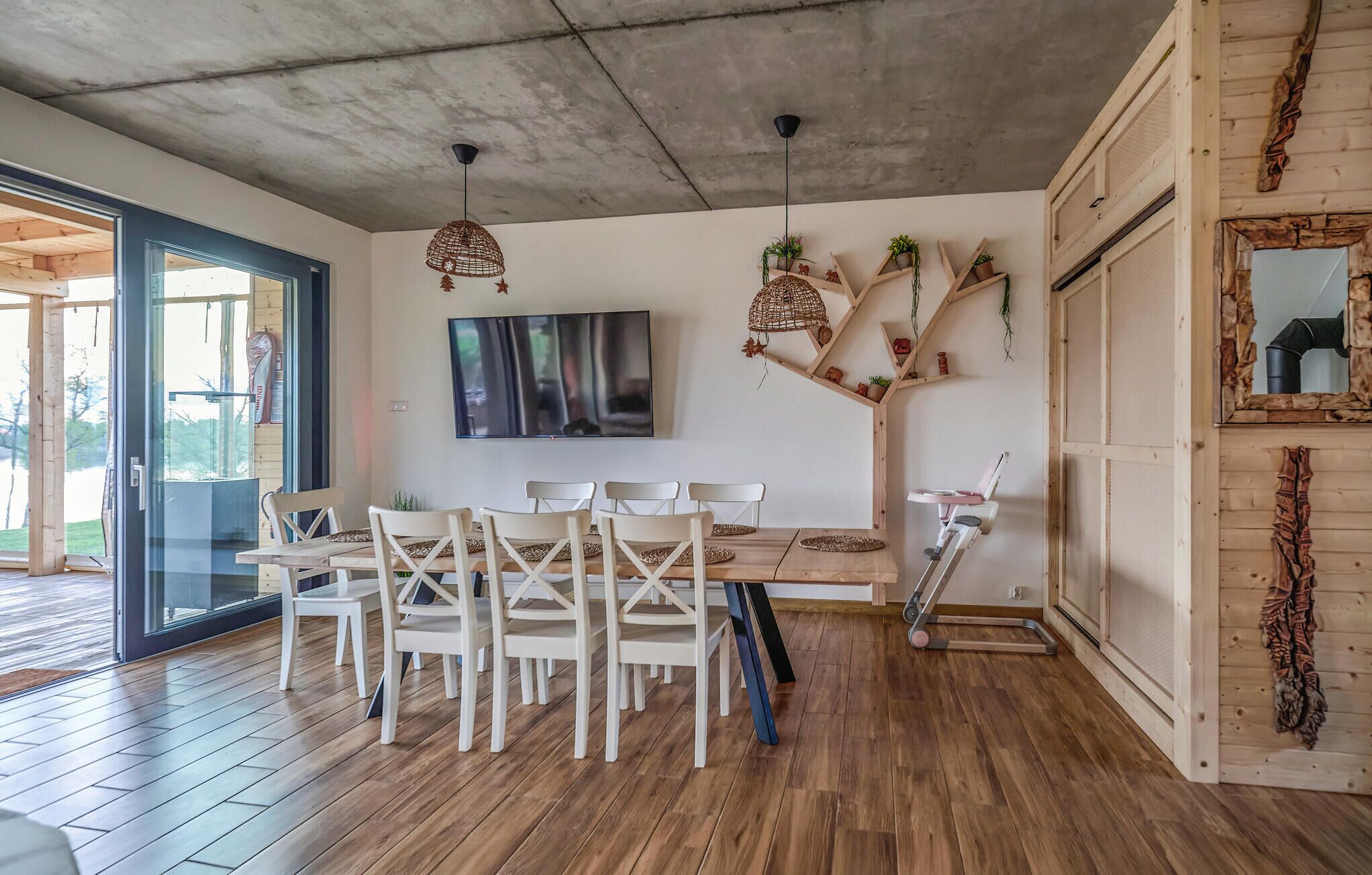 Un espace repas moderne avec une table et des chaises en bois, un téléviseur fixé au mur et un escalier agrémenté de plantes.