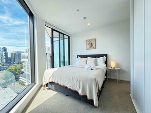 A modern bedroom with a large window, a bed with a headboard, a bedside table with a lamp, and a city view. - Parkside Penthouse 3Beds & 2Baths vs 1AC Pool Gym (Auckland City)