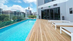 Ein Pool auf dem Dach mit Blick auf die Stadt, ein Glastür-Eingang und eine Holzterrasse.