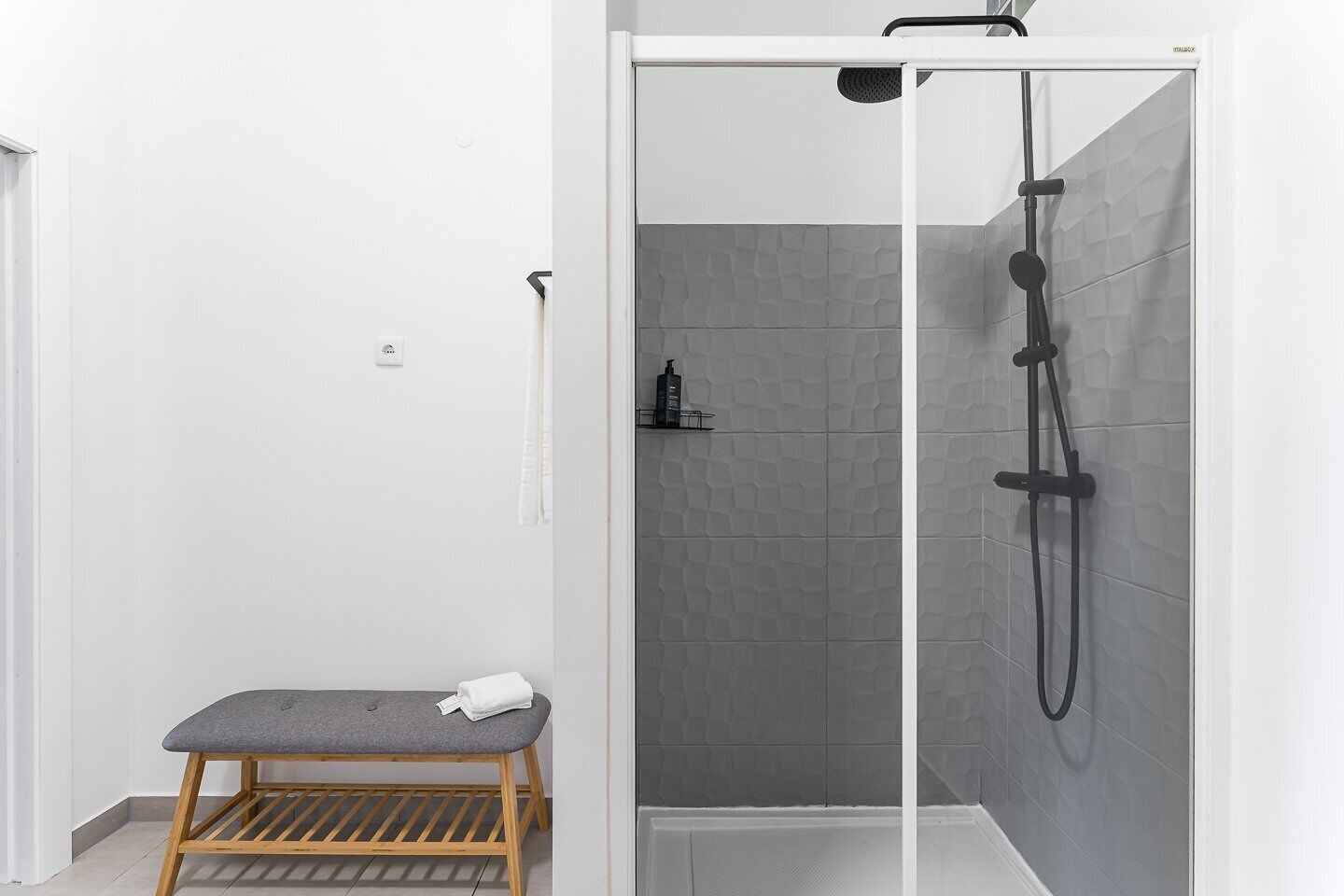 Une douche équipée d’un pommeau de douche à main, d’un banc et d’un mur carrelé.