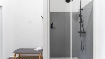 Une douche équipée d’un pommeau de douche à main, d’un banc et d’un mur carrelé.