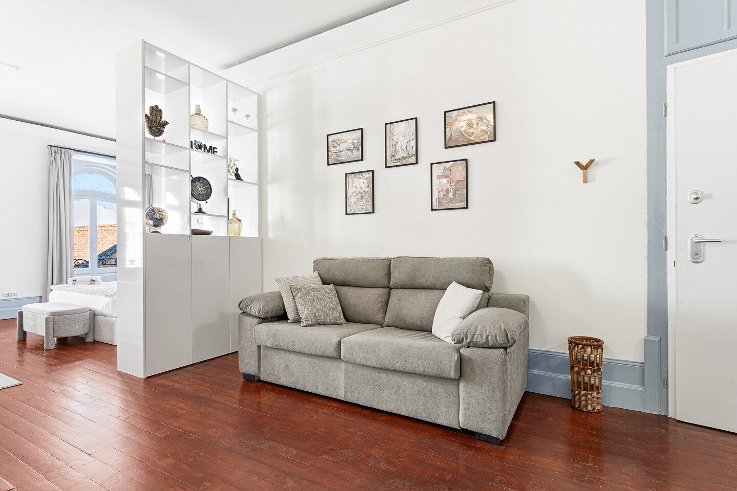 Un salon avec un canapé gris, un meuble blanc avec des étagères et des tableaux encadrés accrochés au mur.