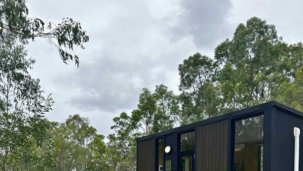 A modern, dark-colored mobile home with a small deck and a fire pit in a grassy area. - Mirror Reflections 2 by Tiny Away (Tamborine)
