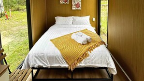 A bedroom with a bed, a wooden floor, a window, and a wall-mounted air conditioner. - Mirror Reflections 2 by Tiny Away (Tamborine)