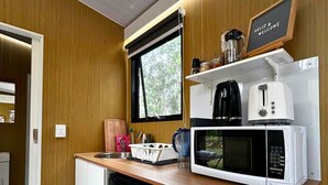 A compact kitchen with a microwave, toaster, and coffee maker on the counter, a window above the sink, and a 'HELLO & WELCOME' sign. - Mirror Reflections 2 by Tiny Away (Tamborine)