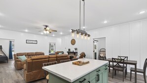 A spacious living area with a sectional sofa, a dining table with chairs, a kitchen island, and a ceiling fan. - Modern Retreat w/ Private Hot Tub & Bunk Room (Jasonville)
