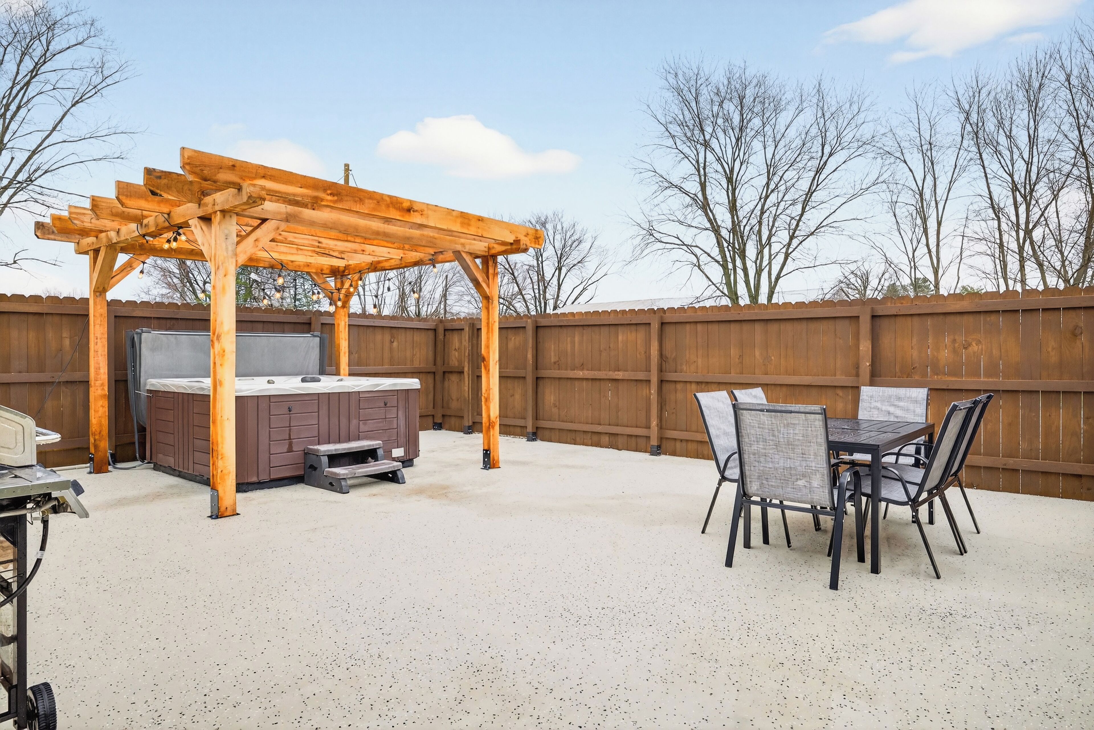 A backyard with a wooden pergola, a hot tub, and a dining table with chairs.