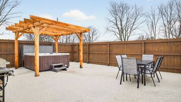 A backyard with a wooden pergola, a hot tub, and a dining table with chairs.