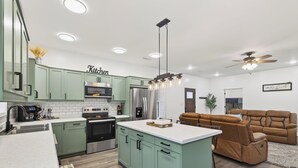 A modern kitchen with green cabinets, a central island, and a dining area with a brown sofa. - Modern Retreat w/ Private Hot Tub & Bunk Room (Jasonville)
