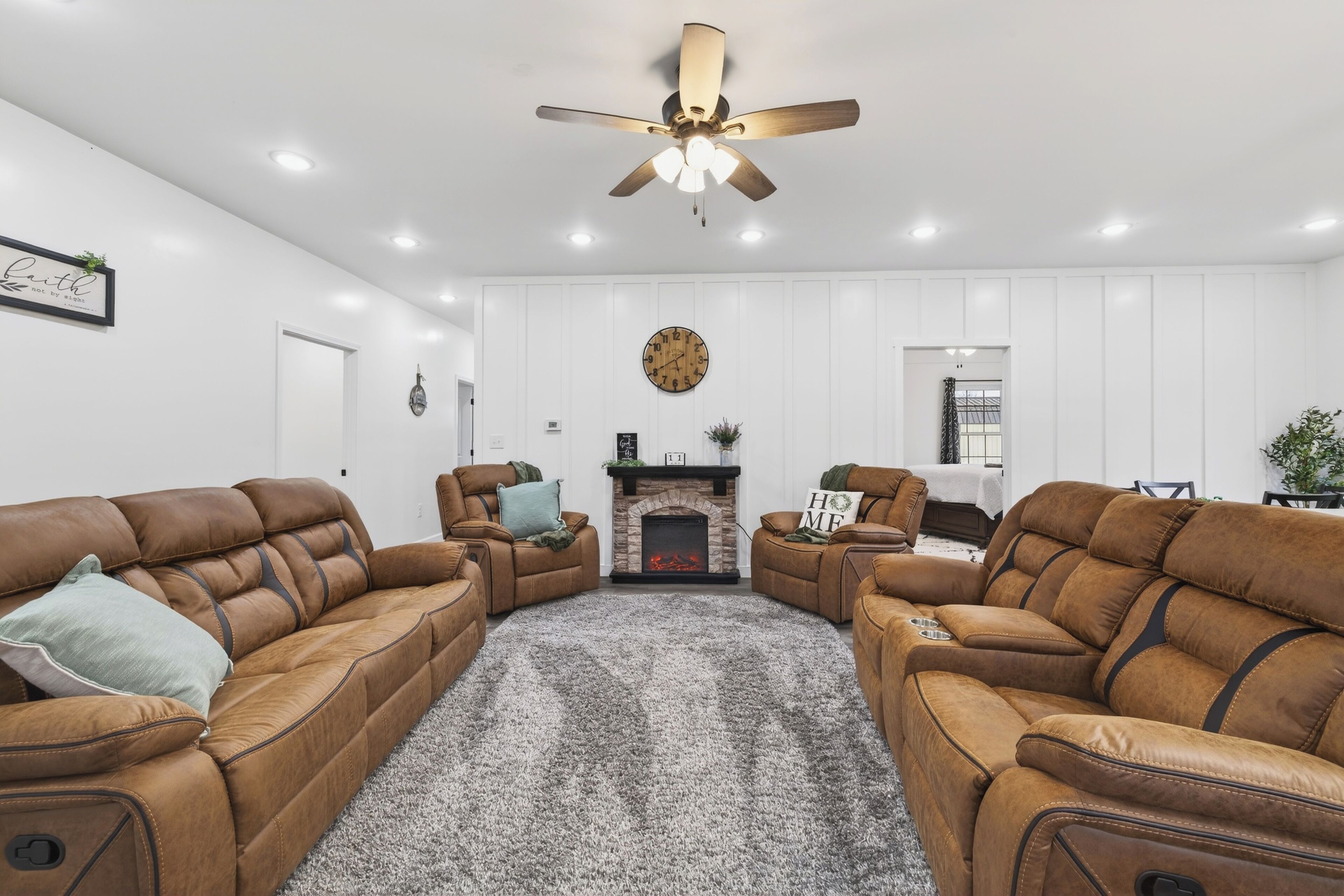A living room with leather sofas, a fireplace, a ceiling fan, and recessed lighting.