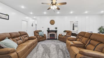 A living room with leather sofas, a fireplace, a ceiling fan, and recessed lighting.