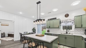 A modern kitchen with a central island, green cabinets, and a kitchen sign. - Modern Retreat w/ Private Hot Tub & Bunk Room (Jasonville)
