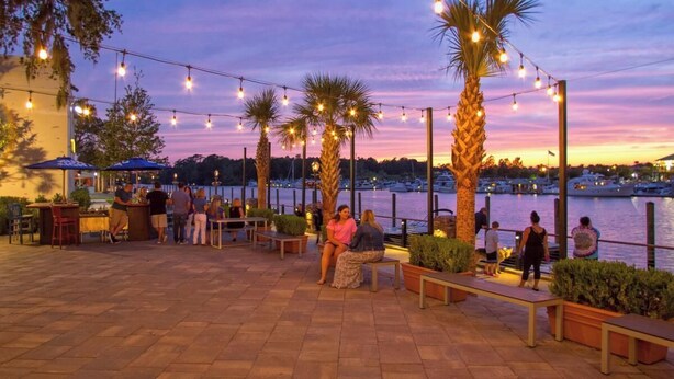 Un patio al aire libre con luces colgantes, palmeras y vista al agua.