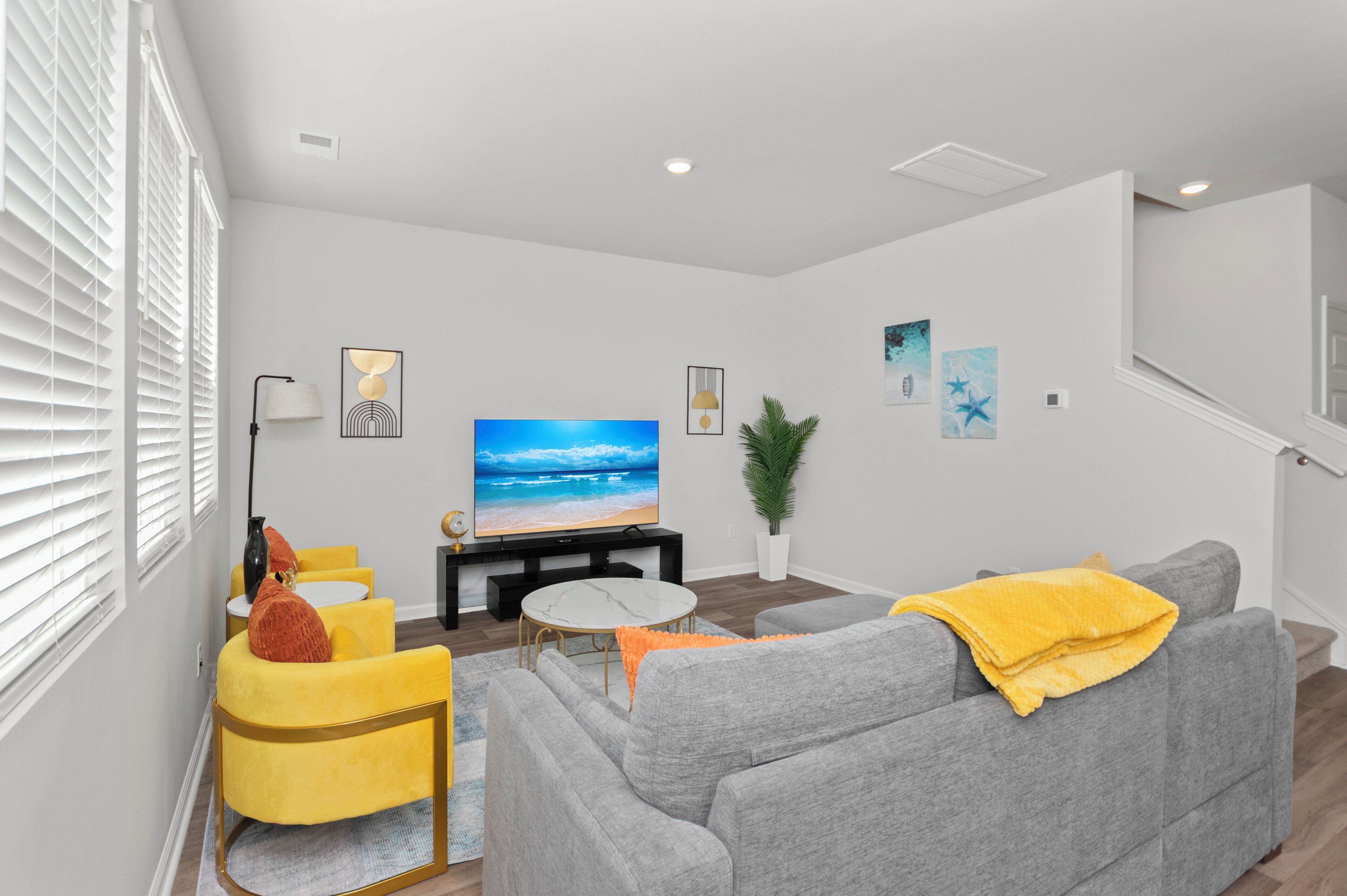 Ein modernes Wohnzimmer mit einem grauen Sofa, gelben Sessel und einem Flachbildfernseher, sowie einer Treppe.