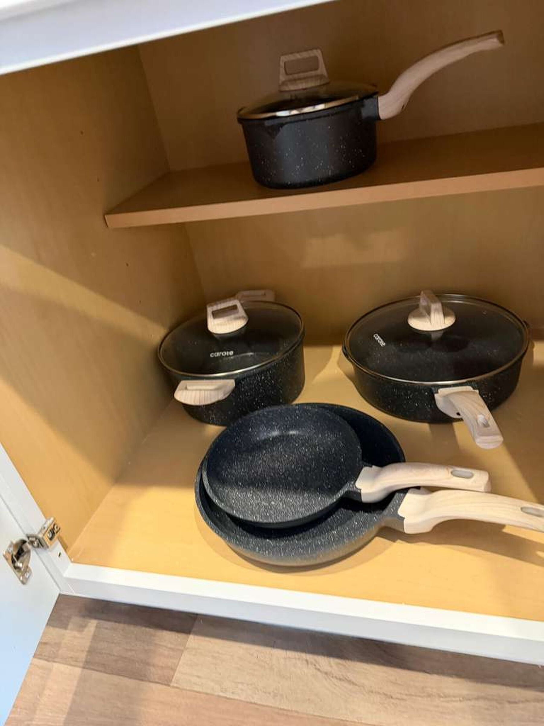 Keittiön kaappi, jossa on kolme mustaa kattilaa ja paistinpannua, ja jokaisessa on valkoinen kahva.