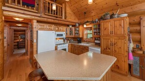 A log cabin interior with a kitchen area, wooden cabinets, a central island, and a dining table. - Otter Point Lodge - 4BR, 3BA 1100ft water frontage log home w/ 2 docks & firepit (Land O' Lakes)