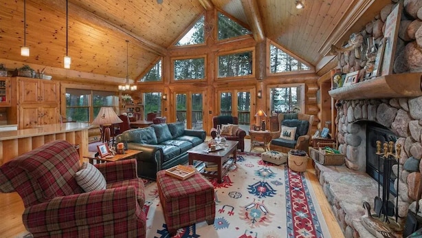 A log cabin interior with a fireplace, leather furniture, and large windows. - Otter Point Lodge - 4BR, 3BA 1100ft water frontage log home w/ 2 docks & firepit (Land O' Lakes)