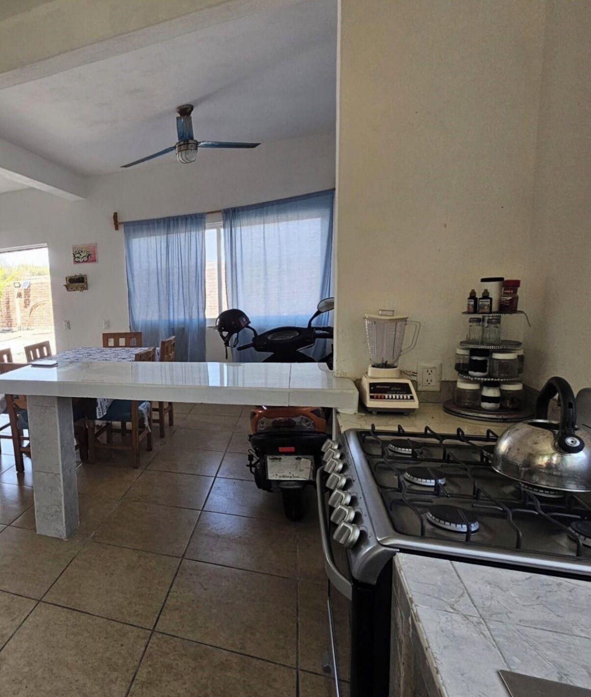 Une cuisine équipée d’une cuisinière à gaz, d’un mixeur et, au fond, une moto.