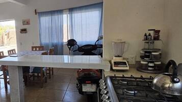 Une cuisine équipée d’une cuisinière à gaz, d’un mixeur et, au fond, une moto.