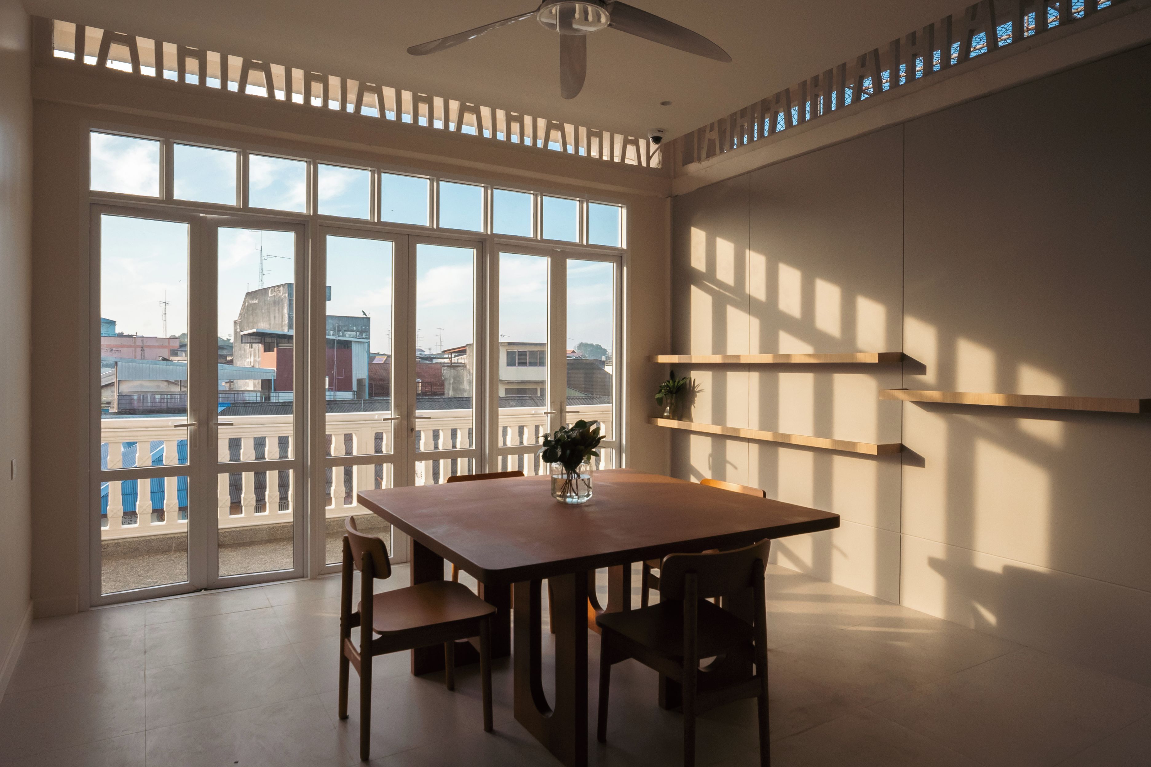 Una habitación con un ventanal grande, ventilador de techo y una mesa con sillas.
