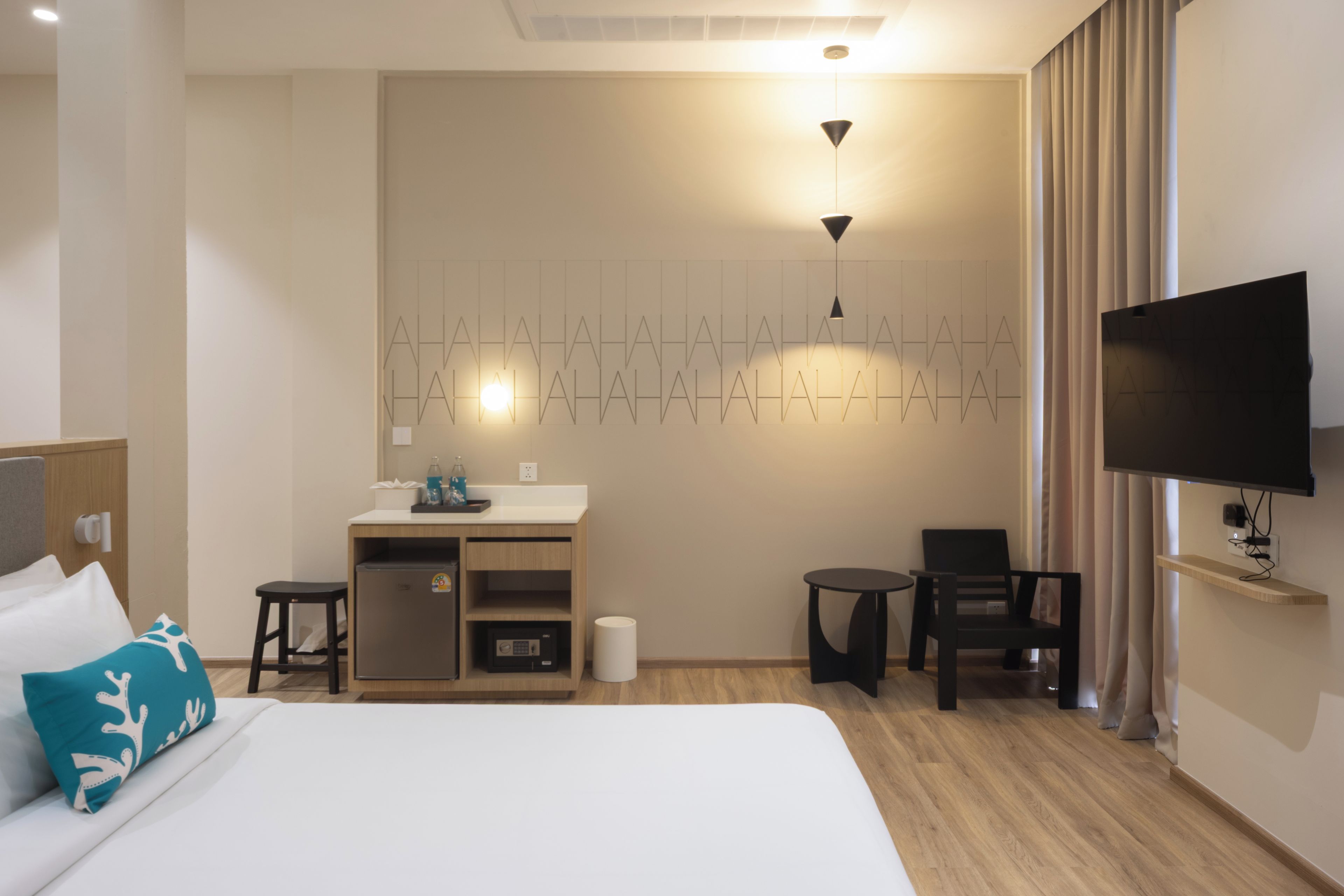 A hotel room with a bed, a desk, a chair, a television, and a wall-mounted light fixture.