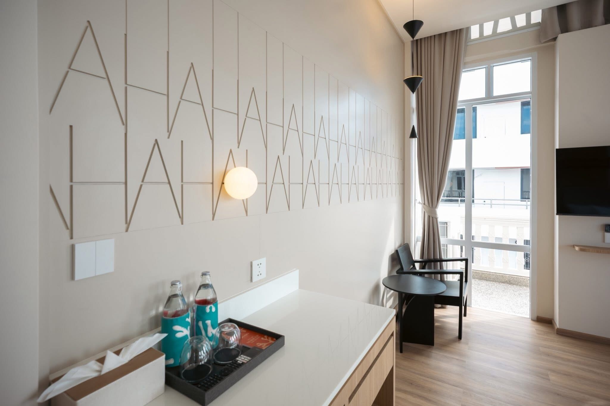 A modern hotel room with a minimalist design, featuring a flat-screen TV, a dining area with a table and chairs, and a decorative wall art installation.