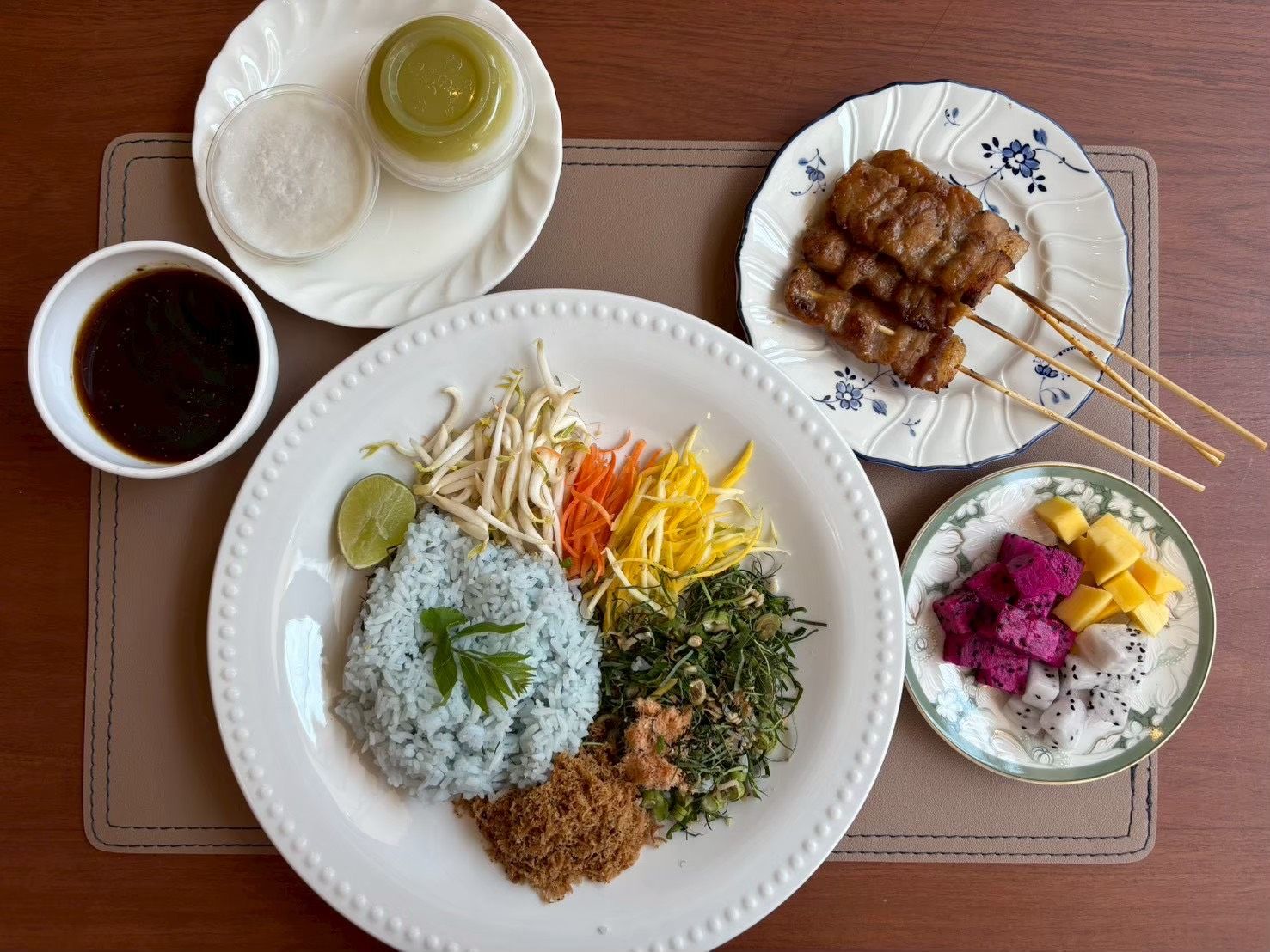 A plate of food with rice, vegetables, and meat, accompanied by a bowl of soup and a plate of skewered meat.