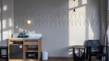 A modern hotel room with a wooden cabinet, a small table, a chair, and a wall-mounted light fixture.