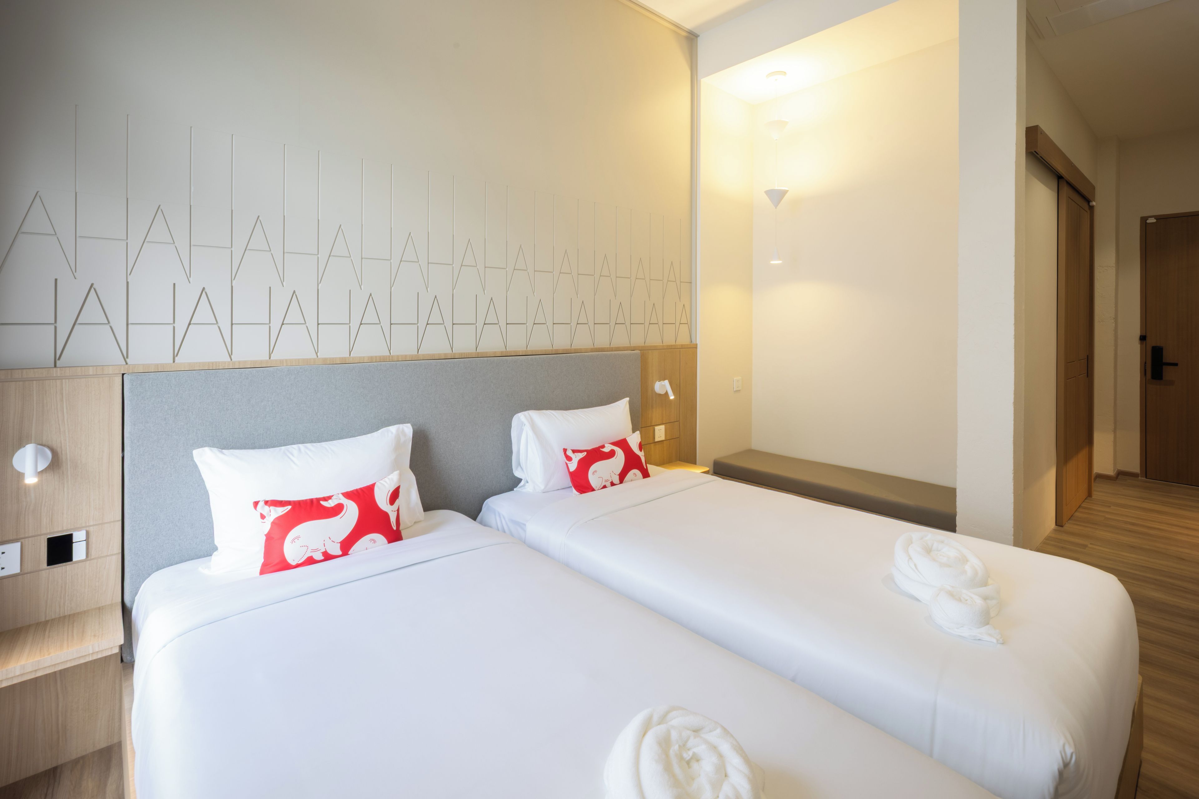 A hotel room with two beds, a wooden headboard, a wall with geometric patterns, and a door leading to another room.