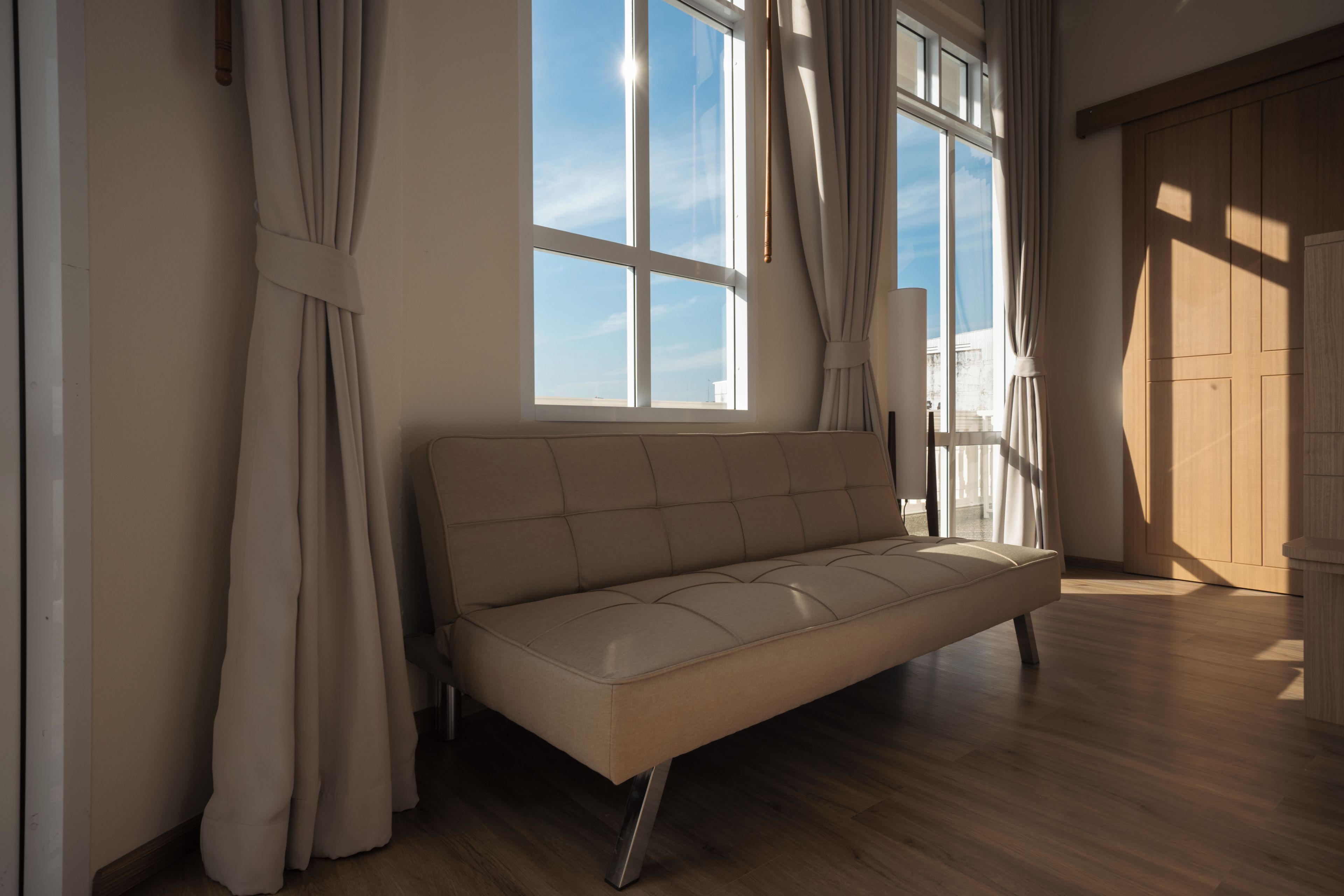 A room with a sofa, large windows, and wooden flooring.