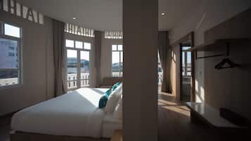 Ein Hotelzimmer mit einem großen Bett, einem Nachttisch, einem Kleiderschrank und Blick auf die Stadt.