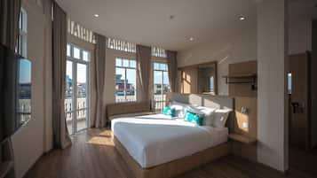 A modern hotel room with a large bed, a flat-screen TV, a wooden headboard, and a balcony with curtains.