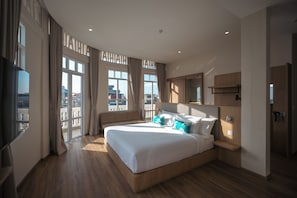 Una habitación de hotel moderna con una cama grande, un televisor de pantalla plana, un cabecero de madera y un balcón con cortinas.
