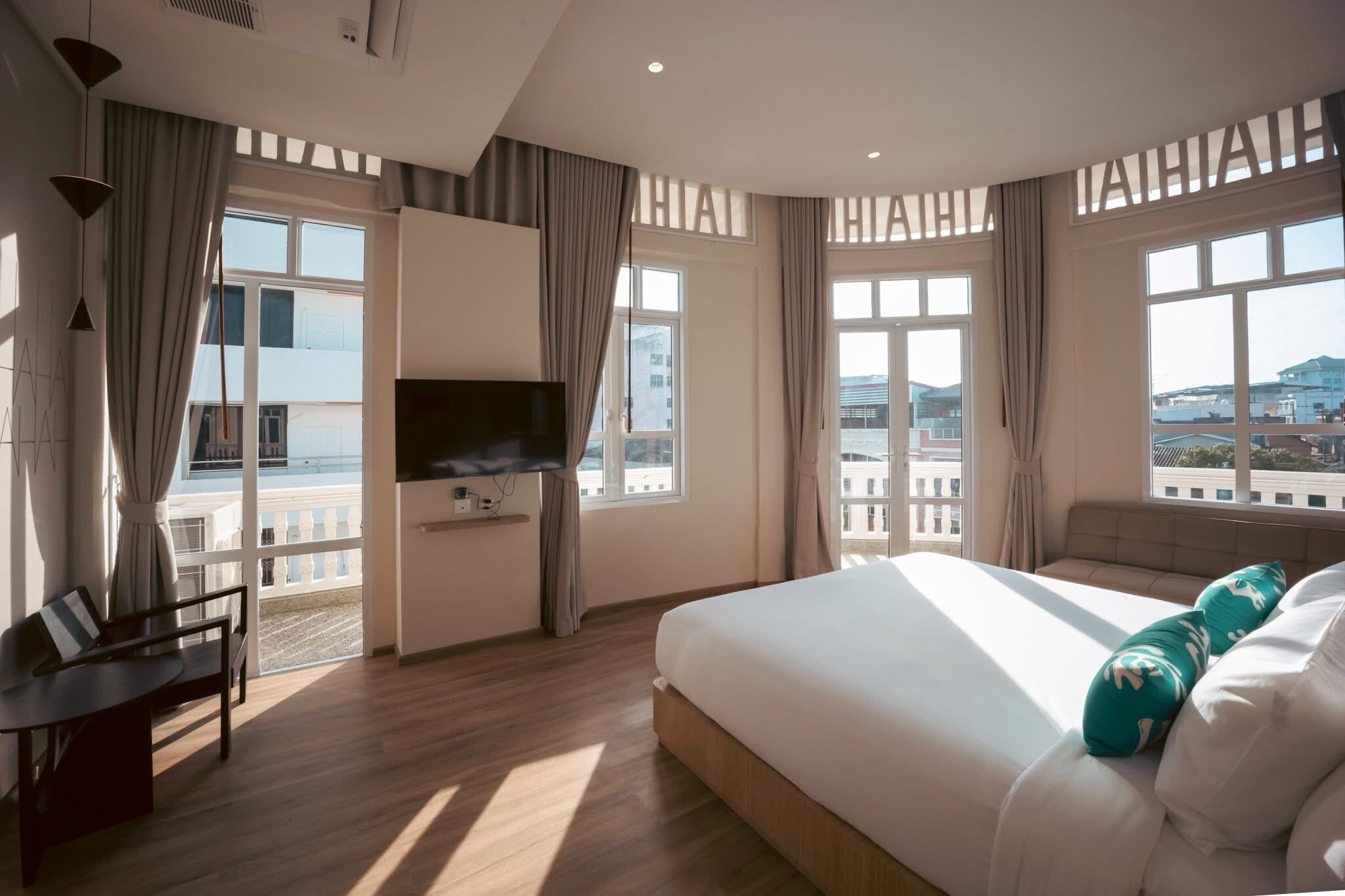 A hotel room with a bed, a desk, a TV, and large windows with a city view.