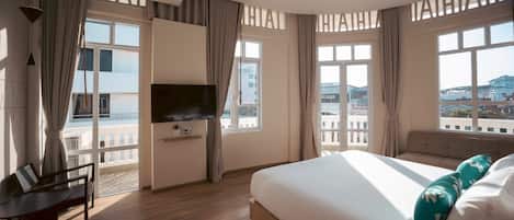 A hotel room with a bed, a desk, a TV, and large windows with a city view.