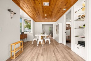 A modern interior with a wooden ceiling, a dining area with white chairs, and a white cabinet with shelves. - Lake Austin Bungalow | Private Dock + Swim Off the Dock (Austin)