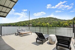 Un balcón con mobiliario exterior, vista a un lago y una colina al fondo.