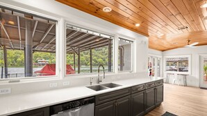 A modern kitchen with a large window, a dishwasher, and a wooden ceiling. - Lake Austin Bungalow | Private Dock + Swim Off the Dock (Austin)
