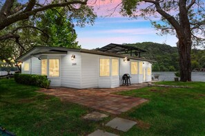 A single-story house with a covered patio, a number '2505' on the side, and a view of a lake. - Lake Austin Bungalow | Private Dock + Swim Off the Dock (Austin)