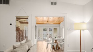 A living room with a sofa, a lamp, and a view of a dining area with chairs and a table. - Lake Austin Bungalow | Private Dock + Swim Off the Dock (Austin)