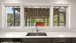 A kitchen with a large window, a sink, and a Bosch dishwasher. - Lake Austin Bungalow | Private Dock + Swim Off the Dock (Austin)