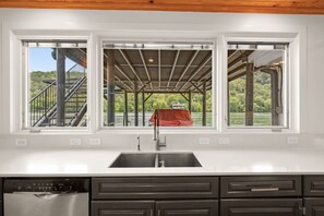 A kitchen with a large window, a built-in dishwasher, and dark cabinetry.