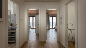 Un couloir doté d’un plancher en bois, de murs blancs et d’un plafond avec des poutres en bois. On y trouve des portes menant à d’autres pièces, un présentoir en métal et un tableau encadré accroché au mur.