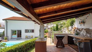 Un espace extérieur abrité comprenant un barbecue, une piscine et une terrasse avec des chaises.