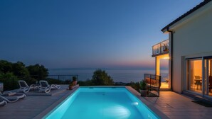 Une piscine avec des chaises longues, un balcon offrant une vue sur la mer et un bâtiment doté de grandes fenêtres.