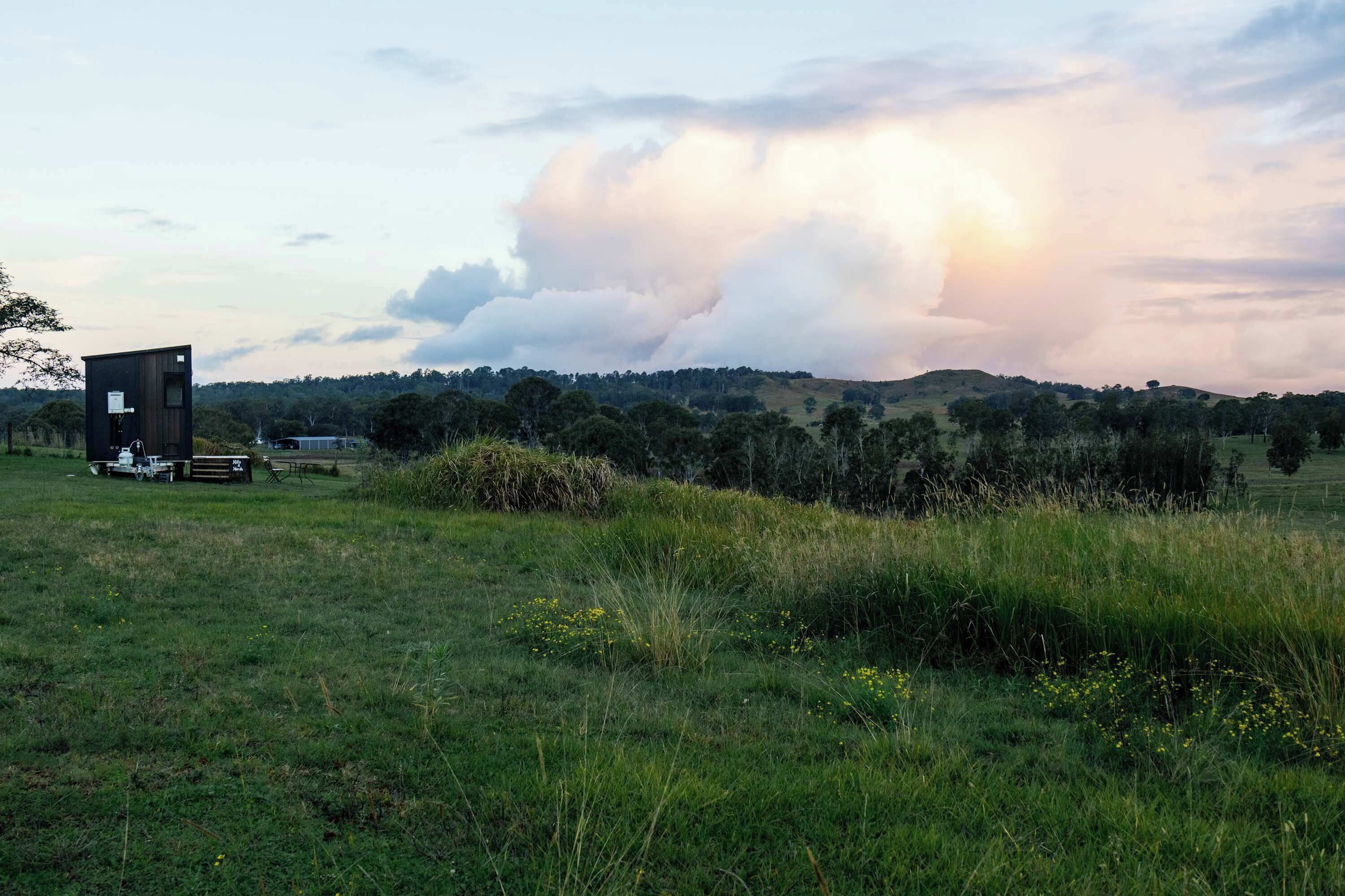 A rural landscape with a small building, open fields, and a cloudy sky.