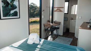 A bedroom with a bed, a chair, a small table, and a view of the outdoors.