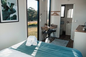 A bedroom with a bed, a chair, a small table, and a view of the outdoors.